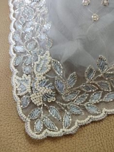 an embroidered piece of cloth with beading and pearls on the edge is laying on a brown surface