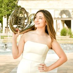 a woman in a white dress is holding a brass instrument