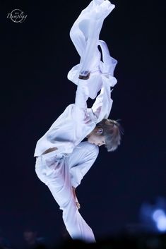 a woman in white performing on stage with one leg up and the other upside down