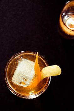 two glasses filled with drinks on top of a black table next to each other and one has an orange peel sticking out of it