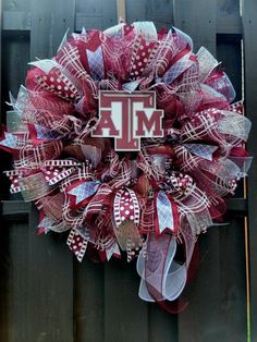 a red and white wreath with the letter m on it's side hanging on a wooden fence