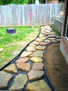 a stone path in the backyard leading to a fenced in area with grass and rocks