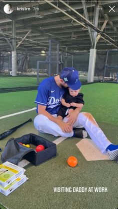 a man holding a child sitting on top of a baseball field next to an orange ball