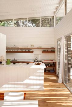 an open kitchen with white walls and wood flooring, along with large windows on the ceiling