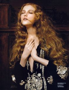 a woman with long, curly hair is wearing a black dress and has her hands on her chest