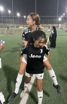 two girls in black and white soccer uniforms are on the field with their arms around each other