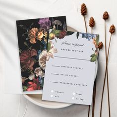 two wedding stationery cards on a plate with pine cones and flowers in the background