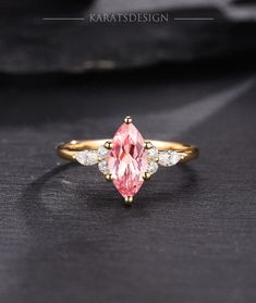 a pink diamond ring sitting on top of a black surface with white diamonds around it