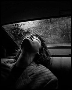 a woman sleeping in the back seat of a car with rain falling down on her head