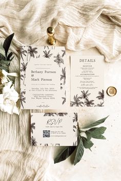 the wedding stationery is laid out on top of a white blanket with greenery