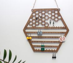 a wall mounted jewelry rack with earrings hanging from it's sides on a white wall next to a potted plant