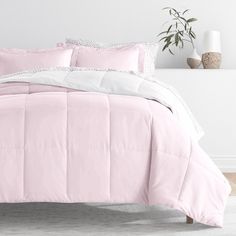 a bed with pink comforter and pillows in a white room next to a potted plant