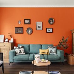 a living room with an orange wall and blue couch in the center, surrounded by pictures on the walls