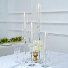 there are many candles on the table with flowers and glasses in front of each other