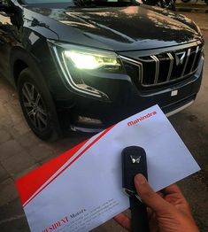 a person holding a car keys next to a black suv with a red stripe on it