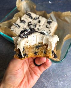 someone holding up a piece of cake with white frosting and chocolate chips on top