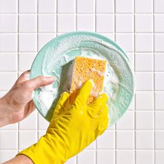 a person in yellow gloves is holding a sponge on a plate with white tiled walls