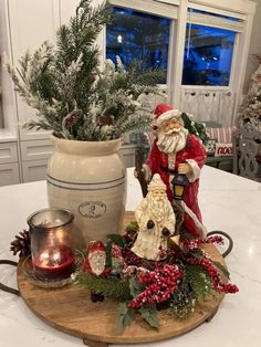 a wooden tray topped with christmas decorations on top of a white kitchen counter next to a potted plant