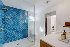 a bathroom with blue tiles on the shower wall and countertop, along with a white toilet