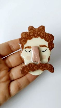 a close up of a person's hand holding a brooch with a mustache