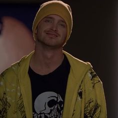 a man in a yellow jacket and skull t - shirt is smiling at the camera