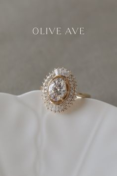 a diamond ring sitting on top of a white cloth with the words olive ave above it