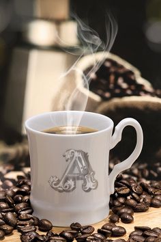 a cup of coffee with steam rising out of it on top of some coffee beans