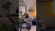 a woman sitting on a couch in a living room next to a table with a potted plant