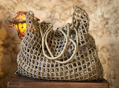 a crocheted purse sitting on top of a wooden table next to a lamp