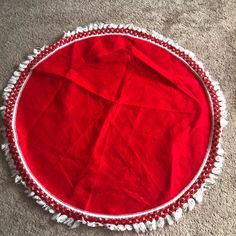 a red and white round rug with tassels on the bottom is laying on the floor