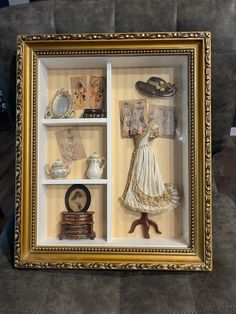 an old fashion doll in a gold framed display case with shoes, hats and other items