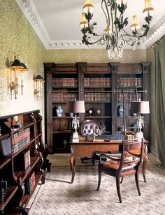 an old fashioned desk in the middle of a room with bookshelves and chandelier