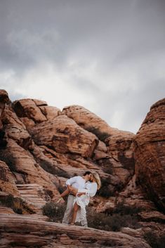 a man and woman embracing in front of some rocks on a cloudy day at the desert