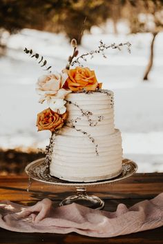 a white wedding cake with flowers on the top is sitting on a table in front of some snow