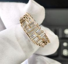 a gold ring with baguette cut diamonds on it's finger, in front of a computer keyboard