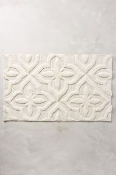 a white bath mat with an intricate design on it's side, against a gray background