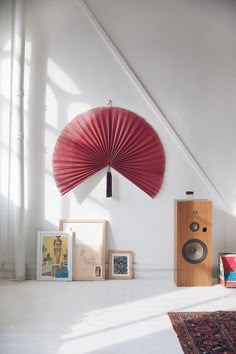 a red fan hanging from the side of a white wall next to a wooden speaker