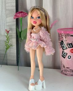 a barbie doll wearing a pink dress and tiara next to a vase with flowers