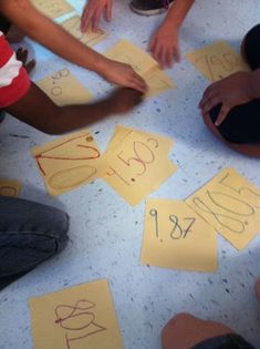 children are sitting on the floor and playing with yellow paper cut out to spell numbers