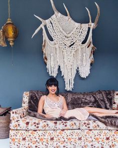 a woman sitting on top of a couch in front of a wall hanging with deer antlers