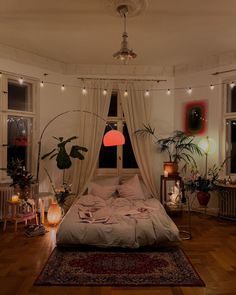 a bed with white sheets and pillows in a room filled with plants, candles and lights