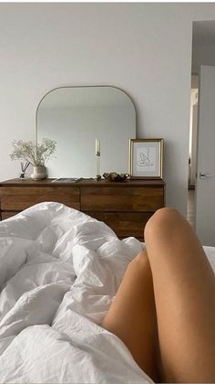 a woman laying on top of a bed under a white comforter next to a dresser