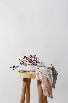 a wooden stool topped with a white and red blanket next to a plant on top of it