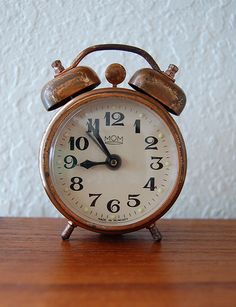 an old fashioned alarm clock sitting on top of a wooden table next to a white wall