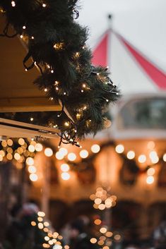 christmas lights are hanging from the roof of a building with a carousel in the background