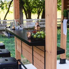 an outdoor bar is set up with copper cups and bowls of fruit on the table