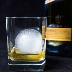 an ice ball in a glass next to a bottle of whisky on a black surface