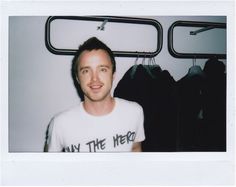 a man in a white shirt standing next to some clothes hanging on a rack and looking at the camera