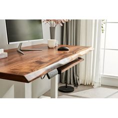 a wooden desk with a computer monitor and keyboard on it, in front of a window