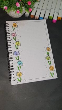 an open notebook with flowers drawn on it next to markers and some pink, yellow, blue, green leaves